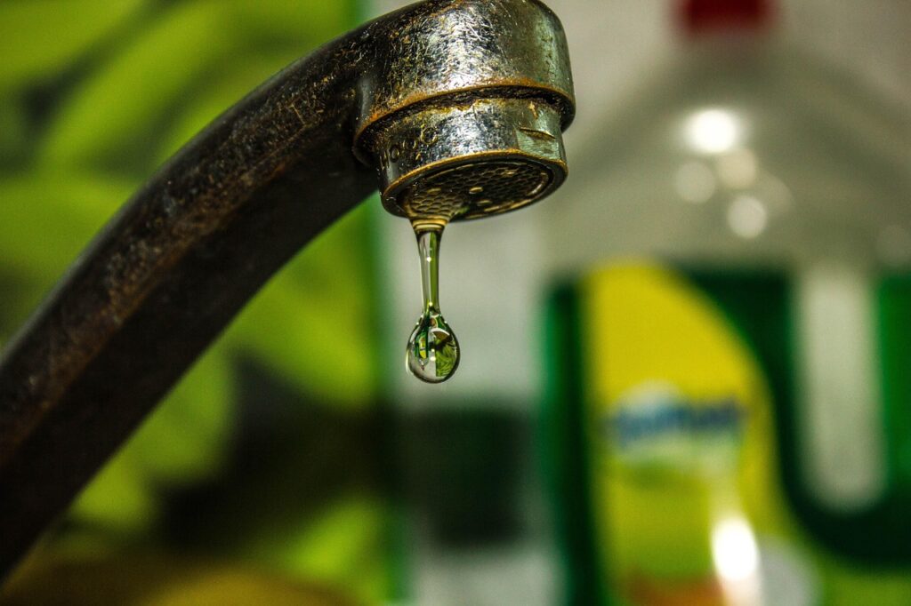Close-up of a dripping faucet, showing potential water waste and contamination risks.