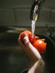 Tomato being washed under running water, highlighting the role of backflow devices in preventing contamination
