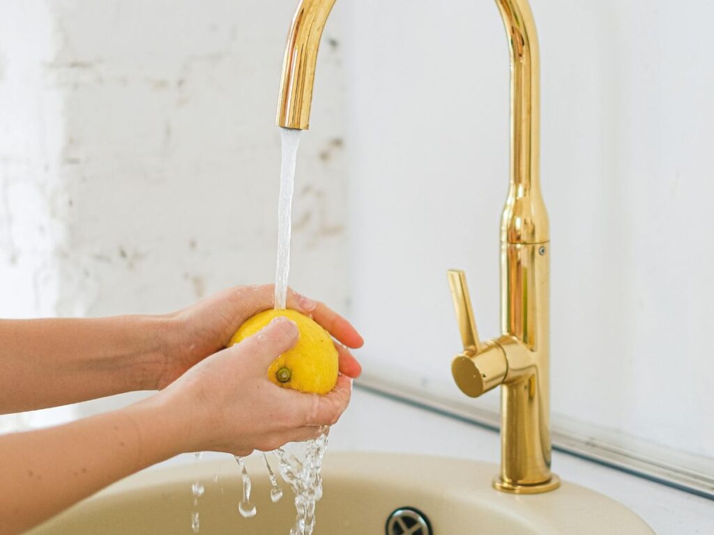 Woman holding lemon under gold faucet – fancy fixtures still need secure plumbing.