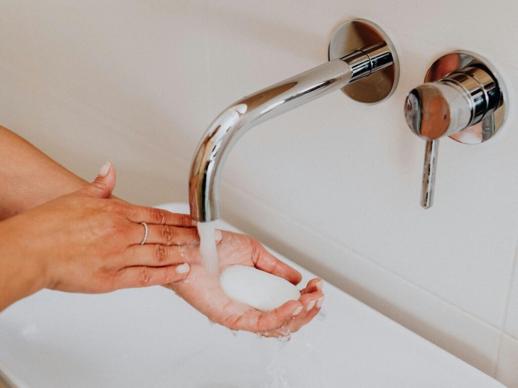 Washing soap bar under wall faucet – older plumbing still needs backflow checks.