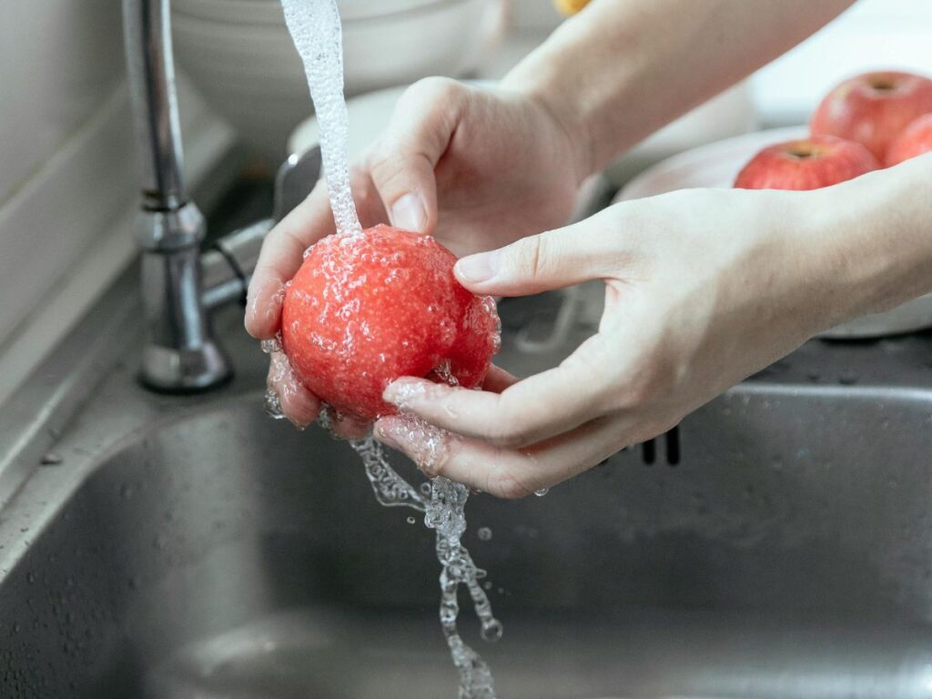 Washing tomato under stream – food prep safety relies on water system integrity.