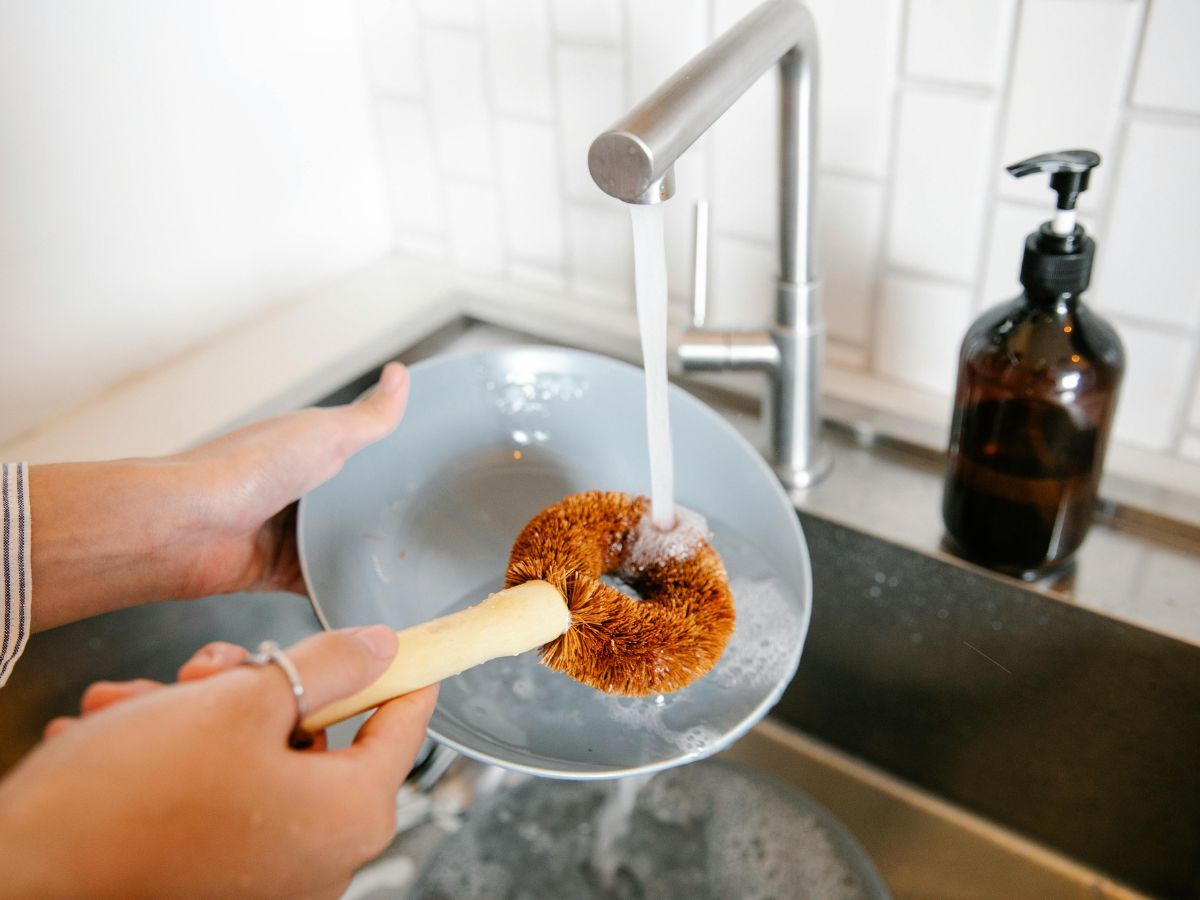 Person cleaning a greasy plate – backflow prevention ensures water used is safe.