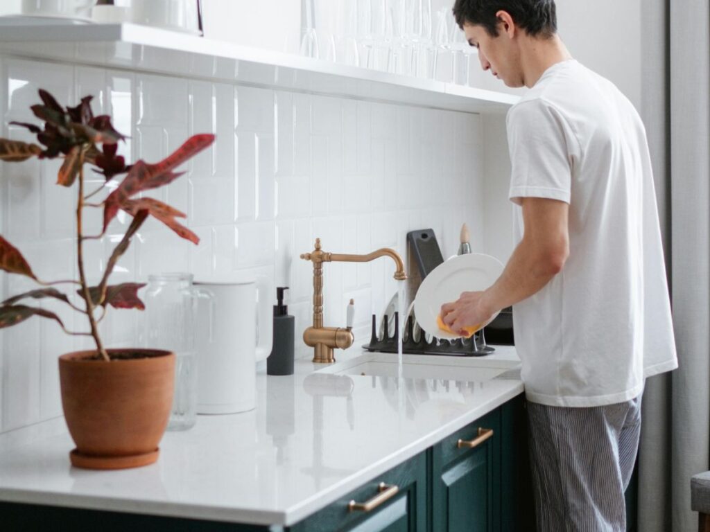 Man washing dishes at home – daily safe water use depends on working plumbing.
